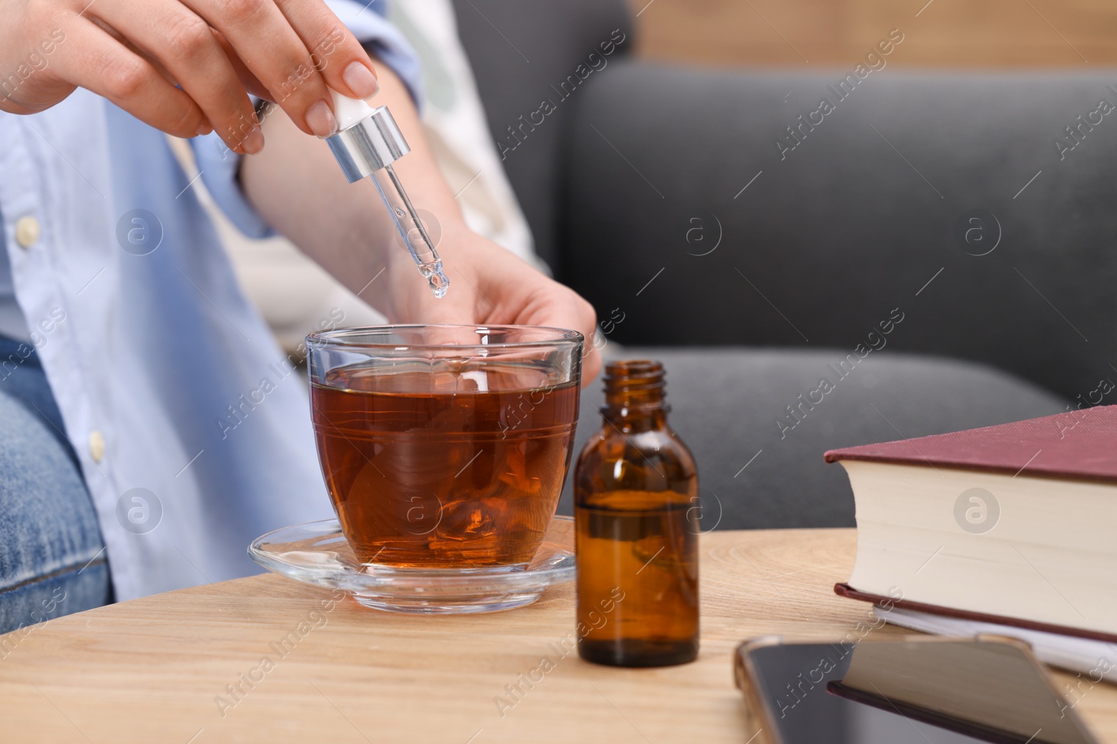 Photo of Woman dripping food supplement into cup of tea at wooden table indoors, closeup