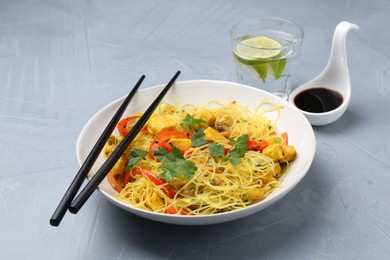 Photo of Stir-fry. Delicious cooked noodles with chicken and vegetables in bowl served on gray textured table