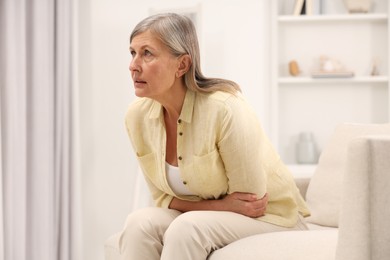 Photo of Menopause. Woman suffering from abdominal pain on sofa at home, space for text