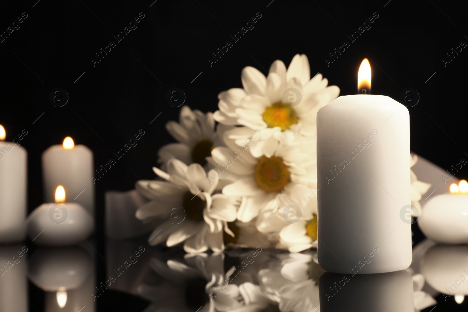 Photo of White chrysanthemum flowers and burning candles on black mirror surface in darkness, space for text. Funeral symbols