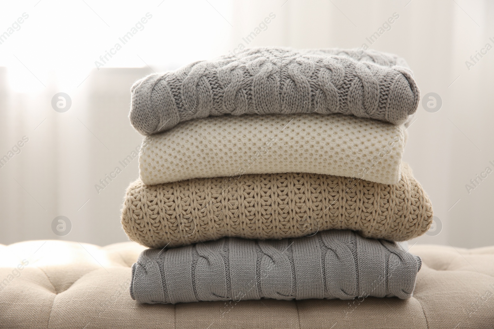 Photo of Stack of folded warm sweaters on couch indoors