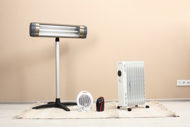 Photo of Different modern electric heaters on floor near beige wall indoors