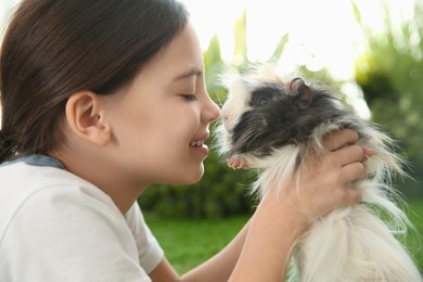Photo of Happy little girl with guinea pig outdoors, closeup. Childhood pet