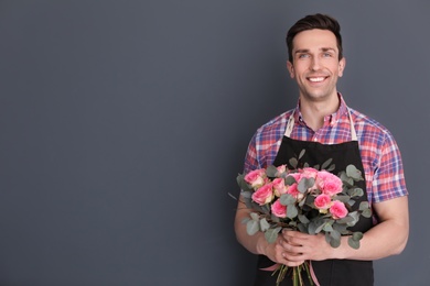 Photo of Male florist holding bouquet of beautiful flowers on dark background