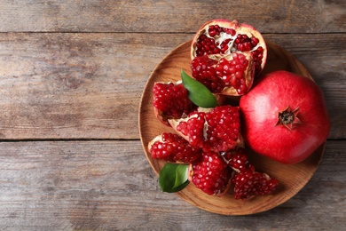 Plate with ripe pomegranates and seeds on wooden background, top view. Space for text