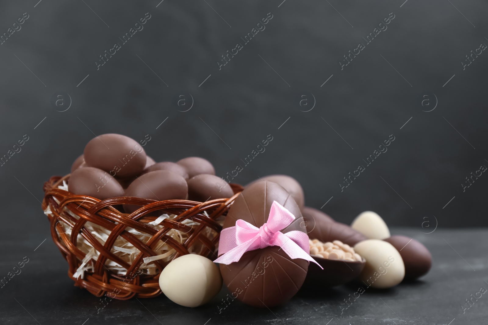 Photo of Sweet chocolate eggs and wicker basket on black table