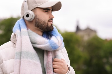 Photo of Handsome man in warm scarf and headphones on blurred background. Space for text