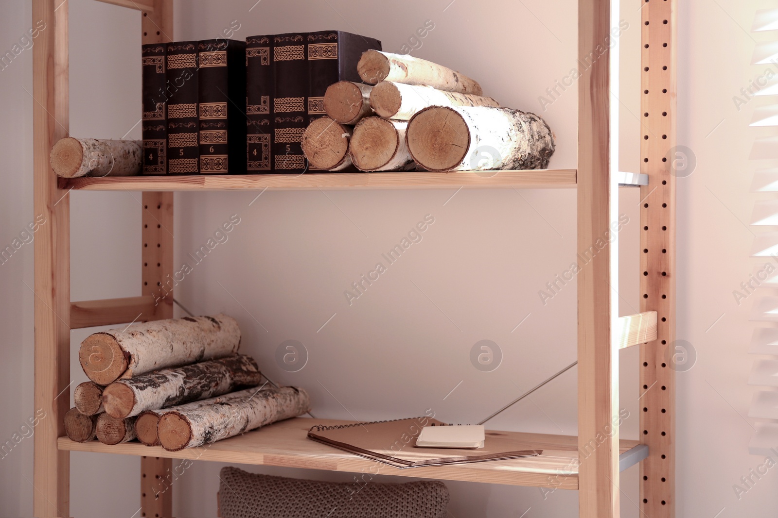 Photo of Shelving unit with stacked firewood and books near wall. Idea for interior design