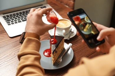 Photo of Male blogger taking photo of dessert and coffee at table in cafe, closeup