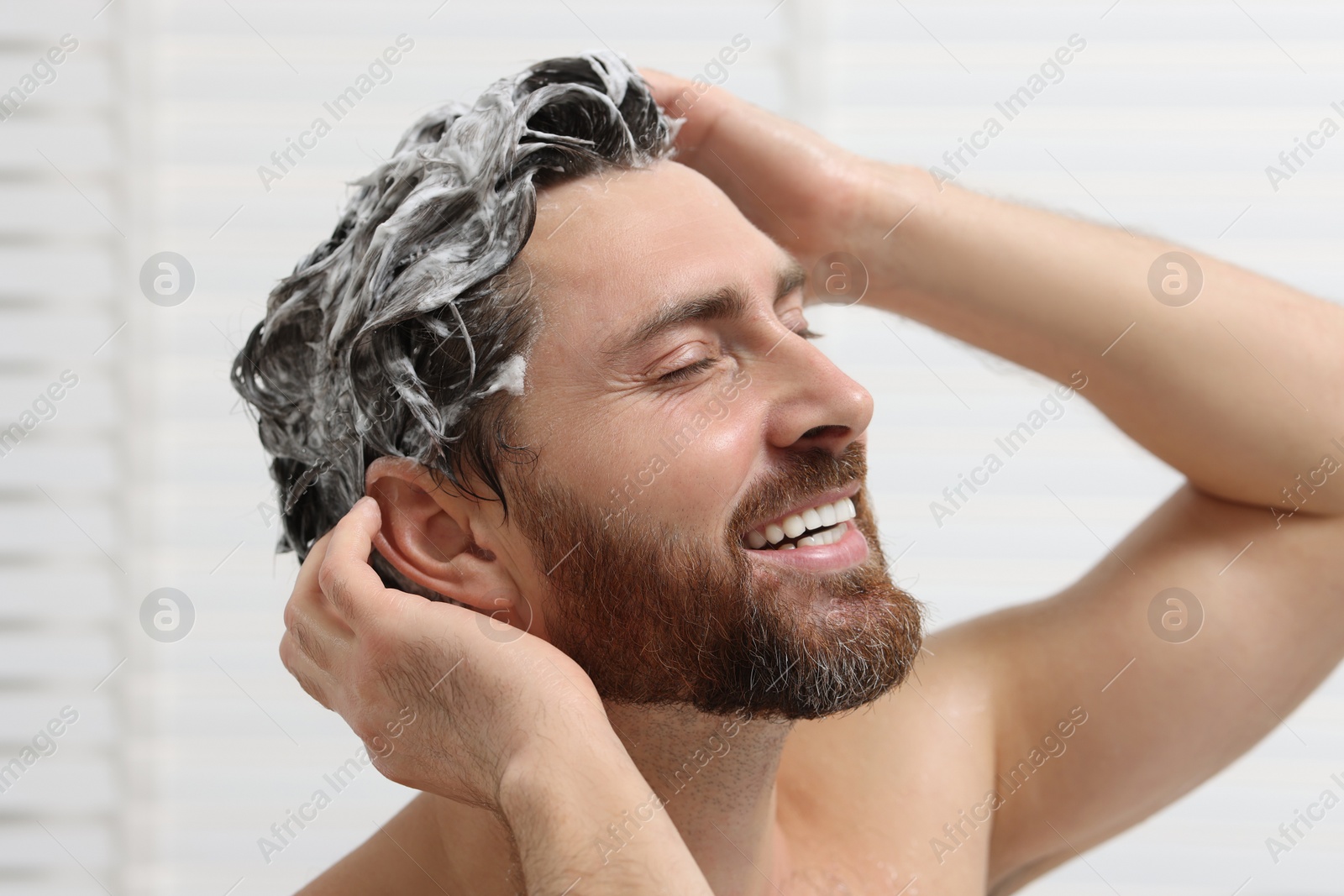 Photo of Happy man washing his hair with shampoo in shower