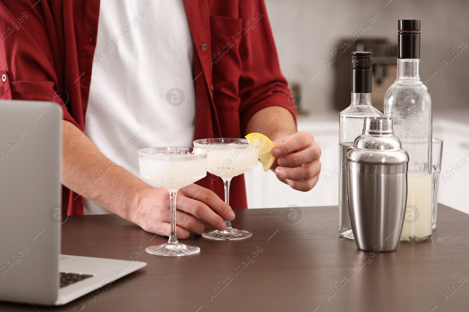 Photo of Man learning to make cocktail with online video on laptop at wooden table in kitchen, closeup. Time for hobby