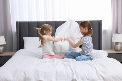 Photo of Cute little sisters having pillow fight on bed at home