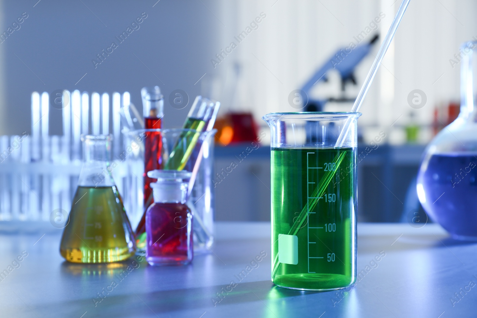 Photo of Beaker with color liquid on table against blurred background, space for text.  Chemistry glassware