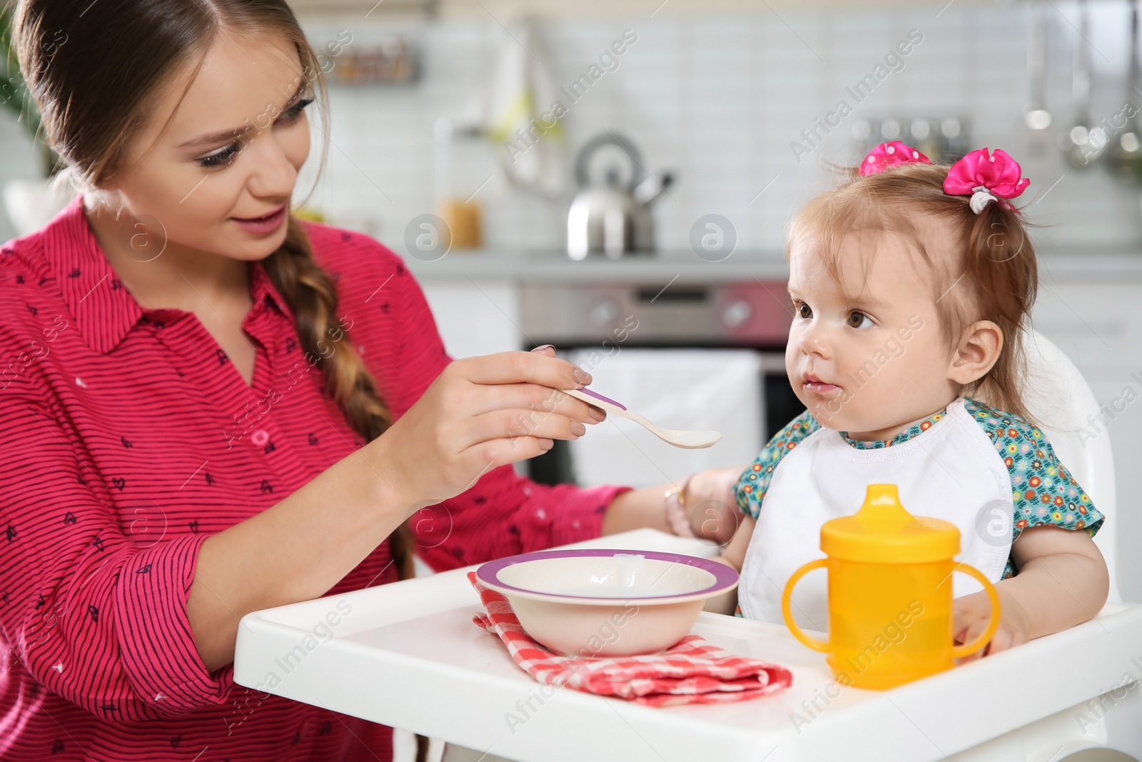 Photo of Mother feeding her little baby with healthy food in kitchen