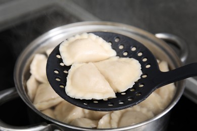 Photo of Dumplings (varenyky) with tasty filling on skimmer over pot indoors, closeup