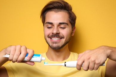 Photo of Portrait of young man with electric toothbrush and paste on color background