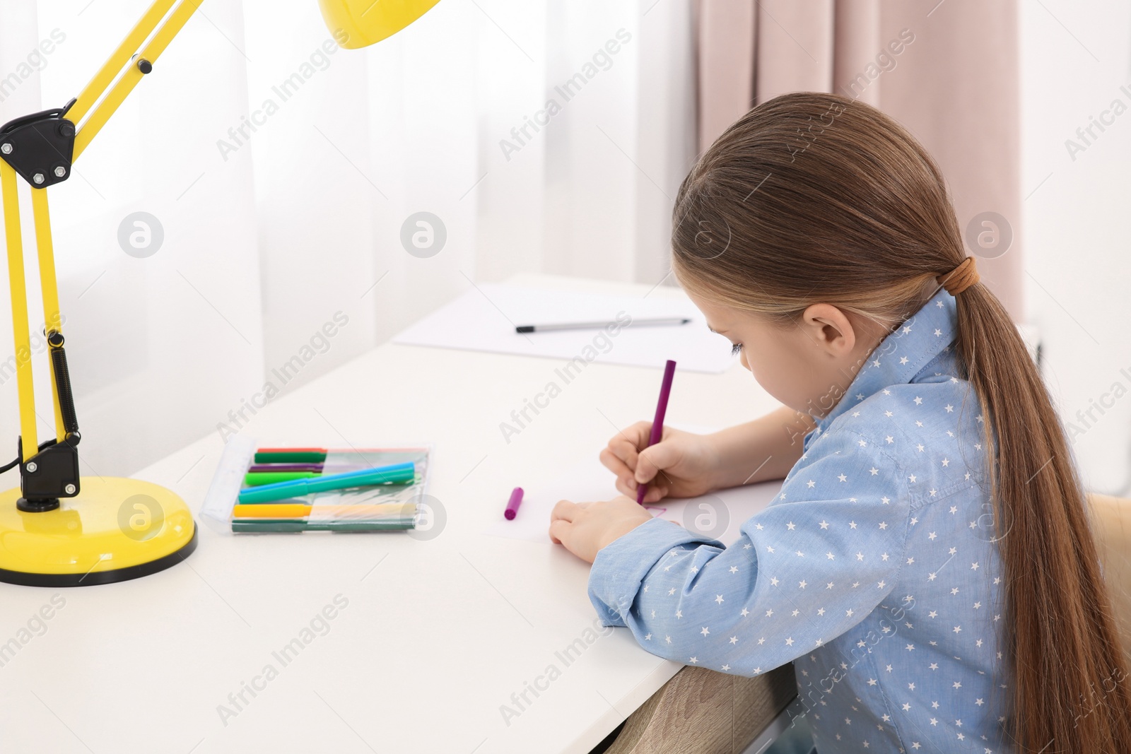 Photo of Cute little girl drawing with marker at desk in room. Home workplace