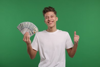 Photo of Happy man with dollar banknotes showing thumb up on green background