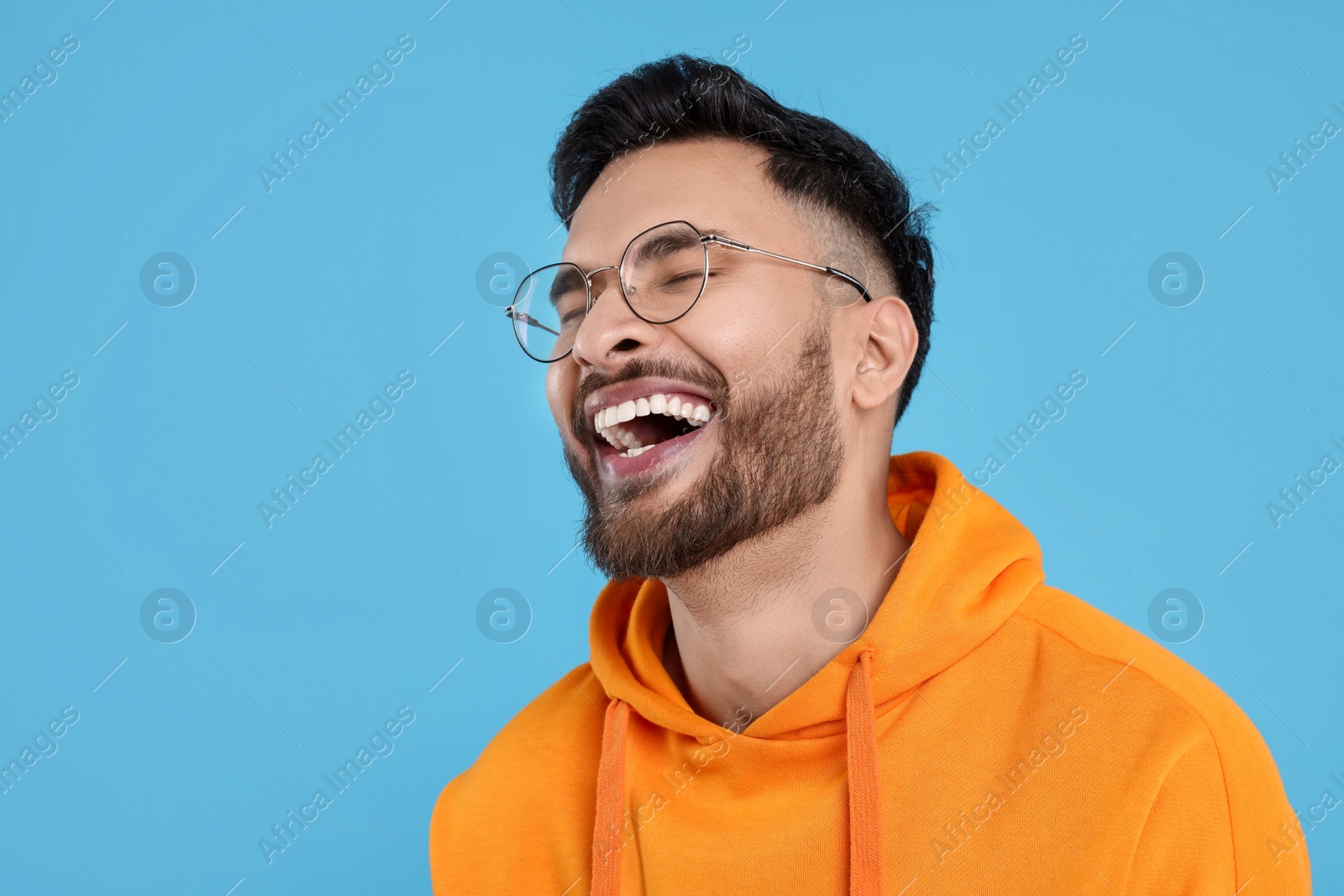 Photo of Handsome young man laughing on light blue background, space for text