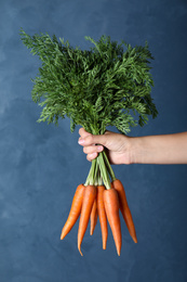 Woman holding ripe carrots on blue background, closeup