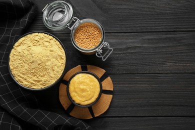 Photo of Flat lay composition with aromatic mustard powder and seeds on black table. Space for text