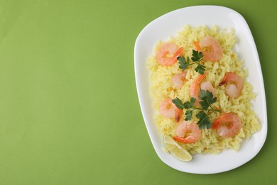 Photo of Delicious risotto with shrimps, lime and parsley on light green background, top view. Space for text