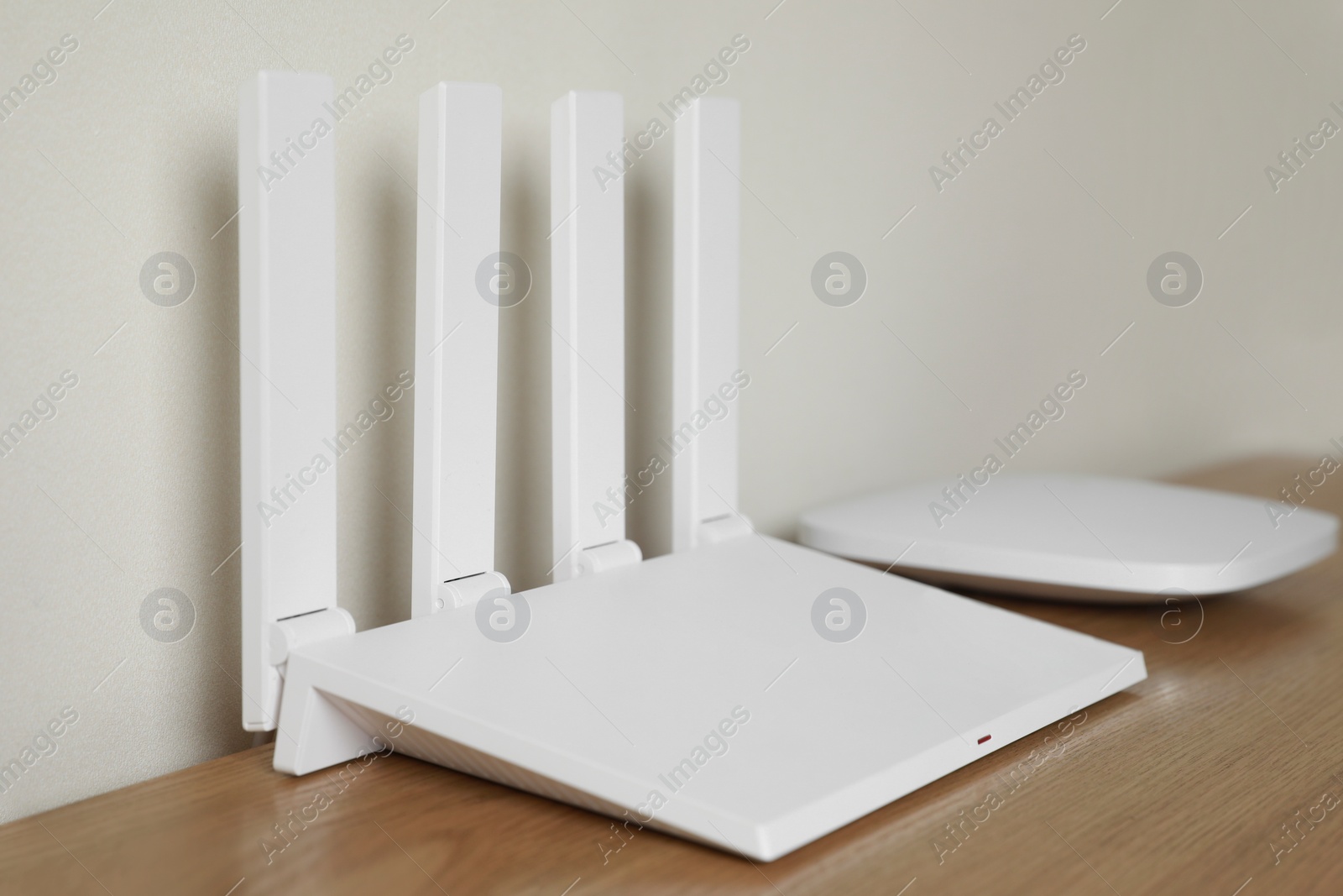 Photo of New modern Wi-Fi router on wooden table near white wall