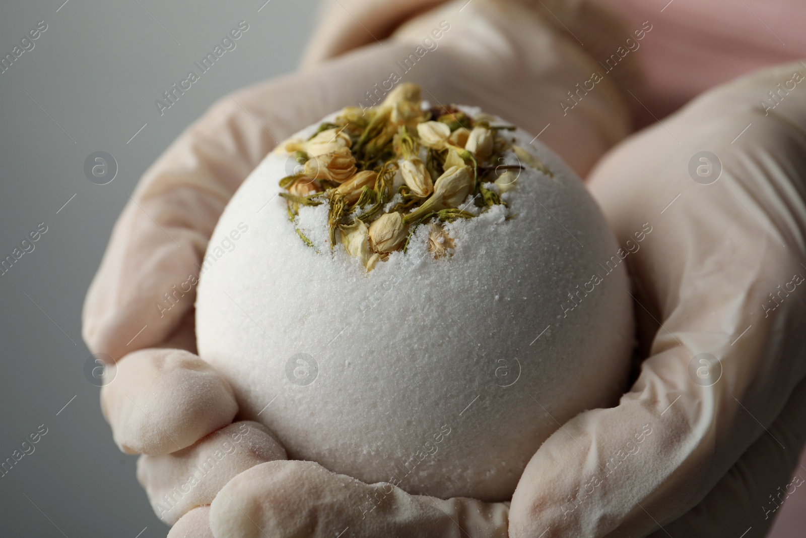 Photo of Woman in gloves with self made bath bomb on grey background, closeup