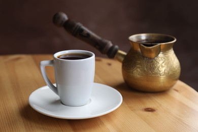 Photo of Turkish coffee. Freshly brewed beverage in cup and cezve on wooden table