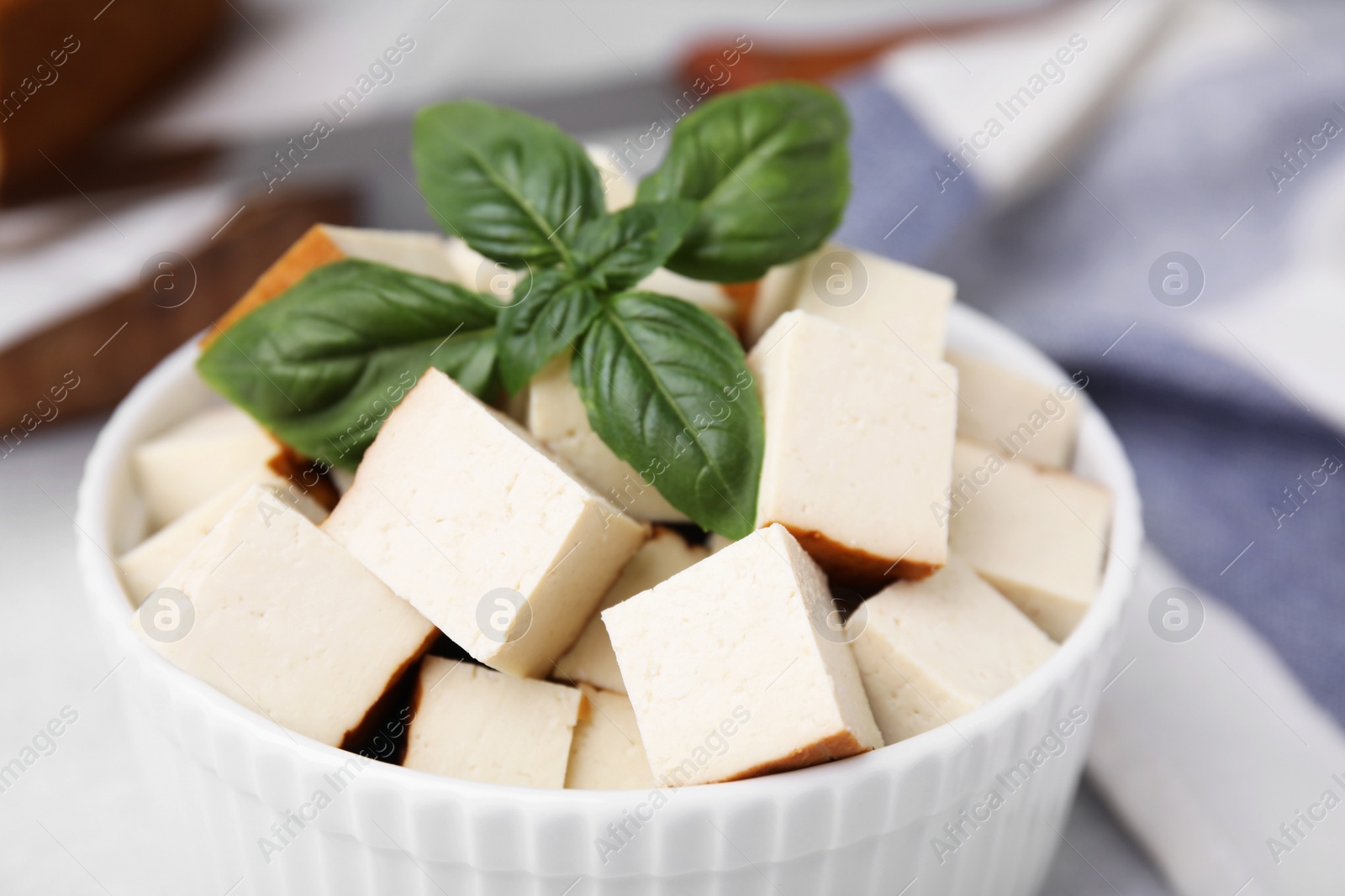 Photo of Bowl of smoked tofu cubes with basil on table, closeup