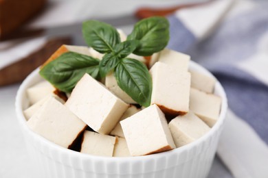 Bowl of smoked tofu cubes with basil on table, closeup