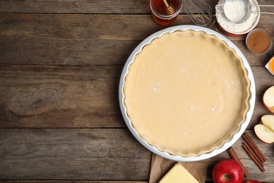 Raw dough and traditional English apple pie ingredients on wooden table, flat lay. Space for text