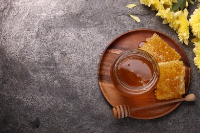 Sweet golden honey in jar, dipper, pieces of honeycomb and chrysanthemum flowers on grey textured table, flat lay. Space for text