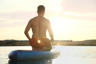 Photo of Man paddle boarding on SUP board in river at sunset, back view