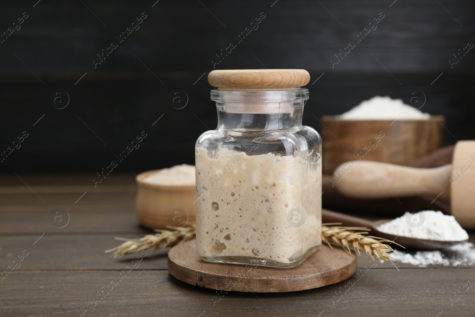 Photo of Leaven, flour and ears of wheat on wooden table