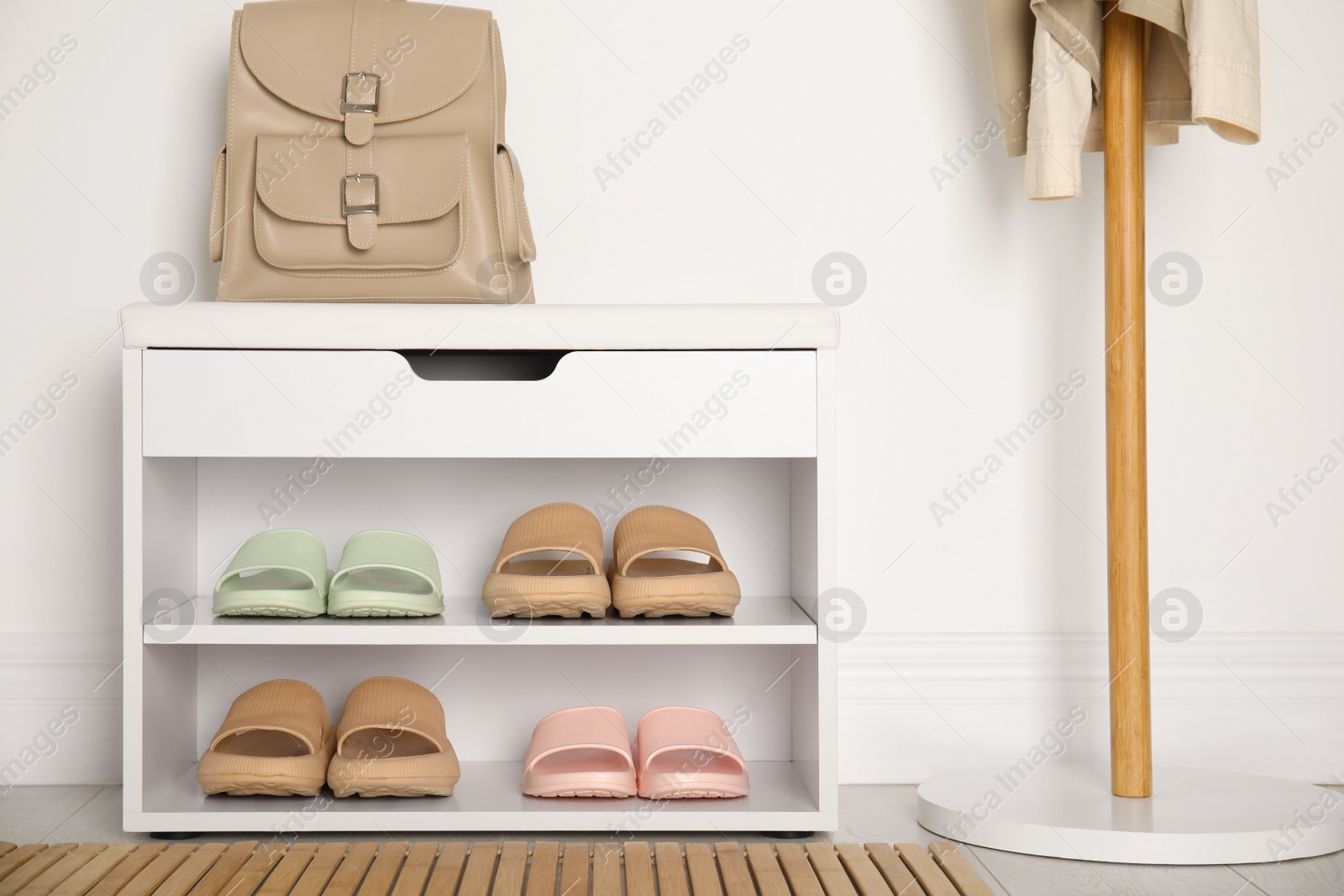 Photo of Storage cabinet with different pairs of rubber slippers near white wall in room