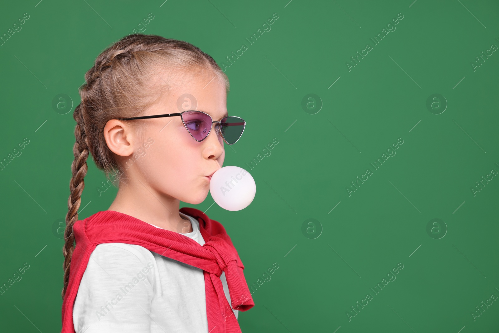 Photo of Girl in sunglasses blowing bubble gum on green background, space for text