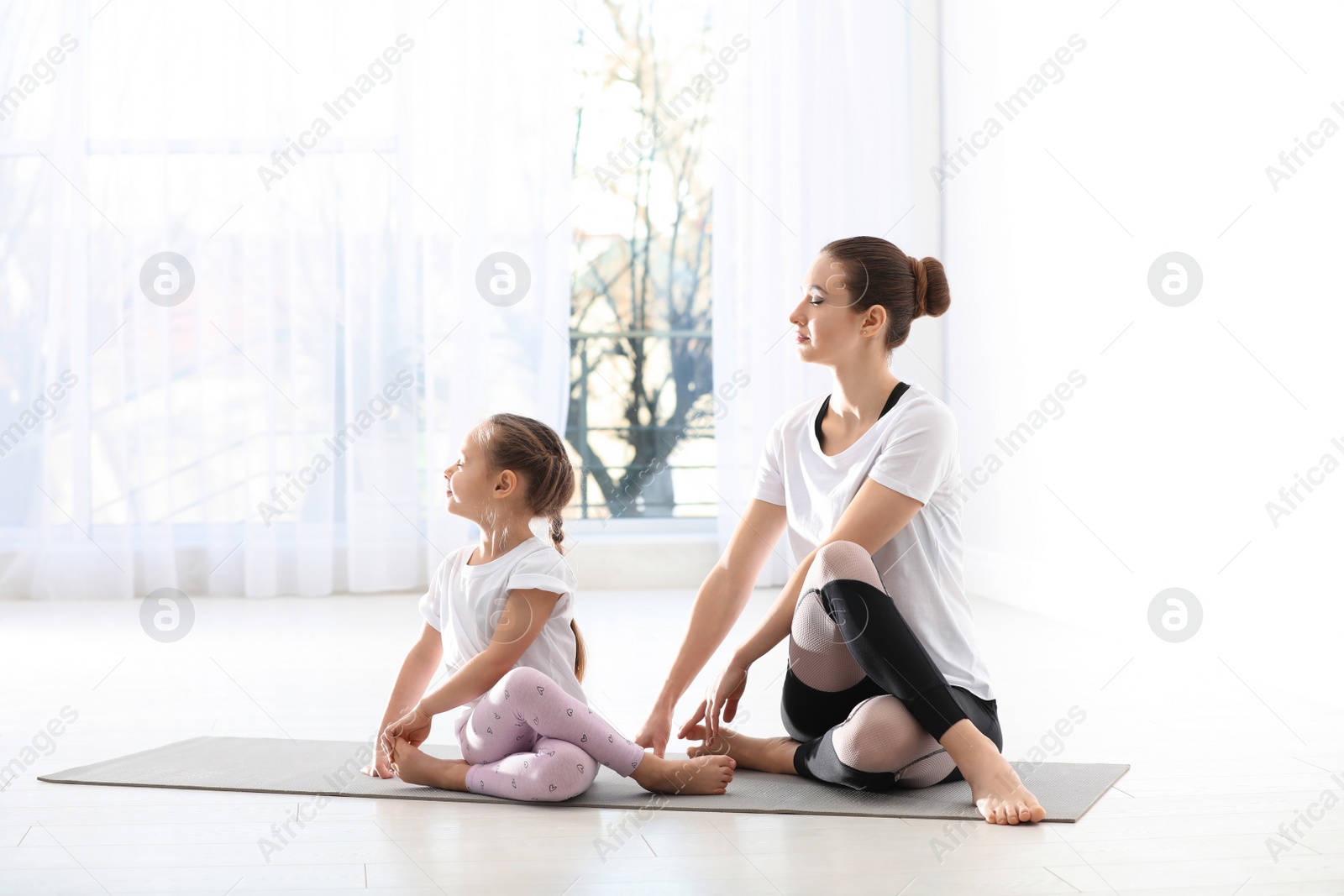 Photo of Young mother with little daughter practicing yoga at home