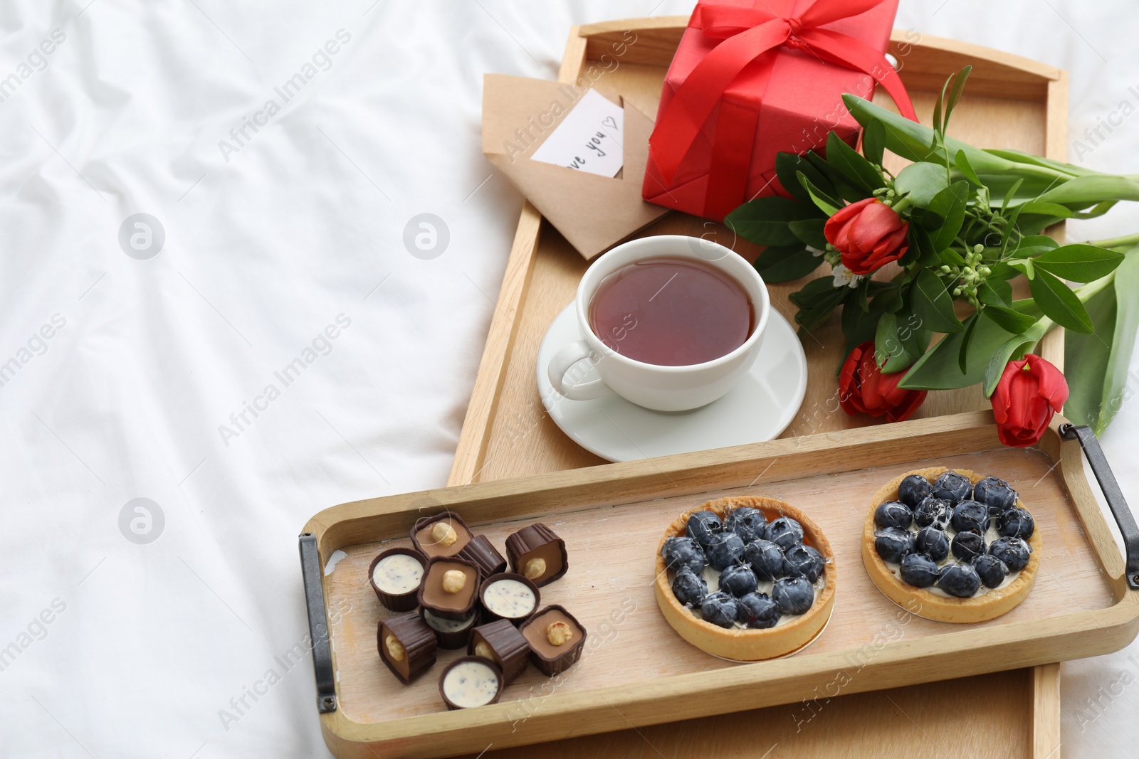 Photo of Tasty breakfast served in bed. Delicious desserts, tea, flowers and gift box on tray, space for text