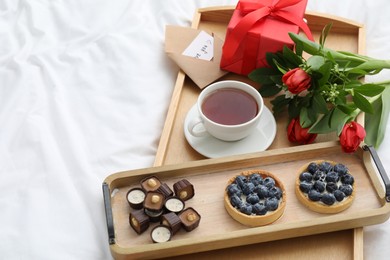 Photo of Tasty breakfast served in bed. Delicious desserts, tea, flowers and gift box on tray, space for text