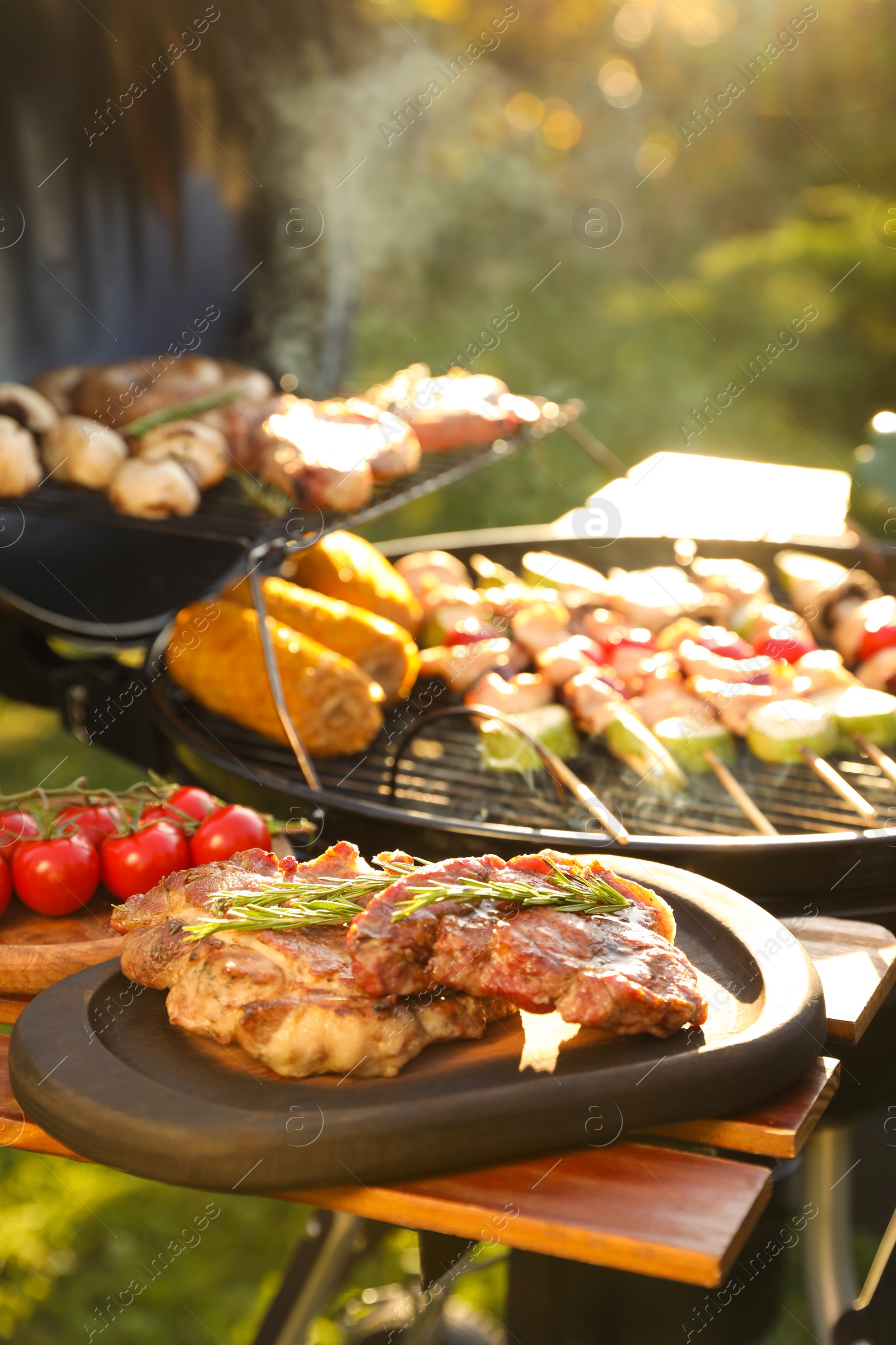 Photo of Tasty cooked meat and cherry tomatoes on table near barbecue grill outdoors