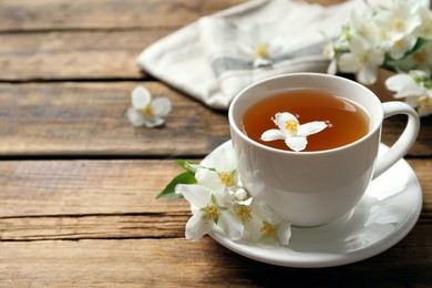 Photo of Cup of aromatic jasmine tea and fresh flowers on wooden table, space for text
