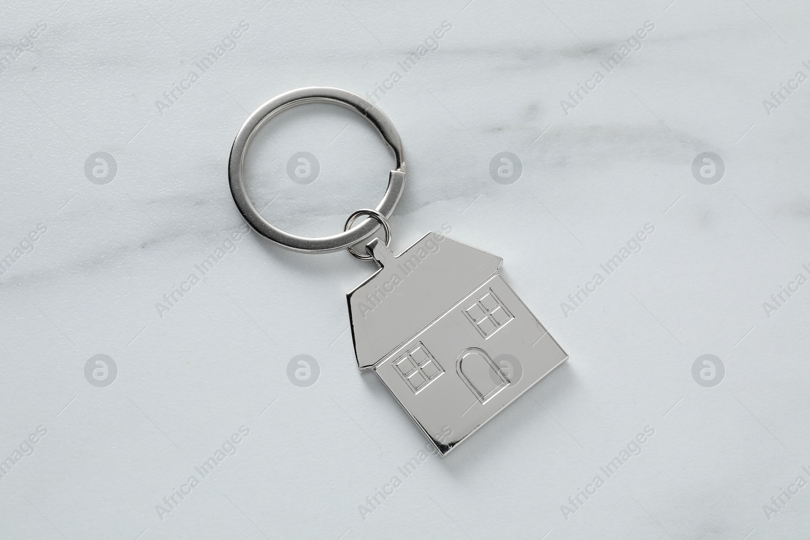 Photo of Metal keychain in shape of house on marble table, top view