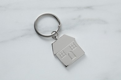 Metal keychain in shape of house on marble table, top view