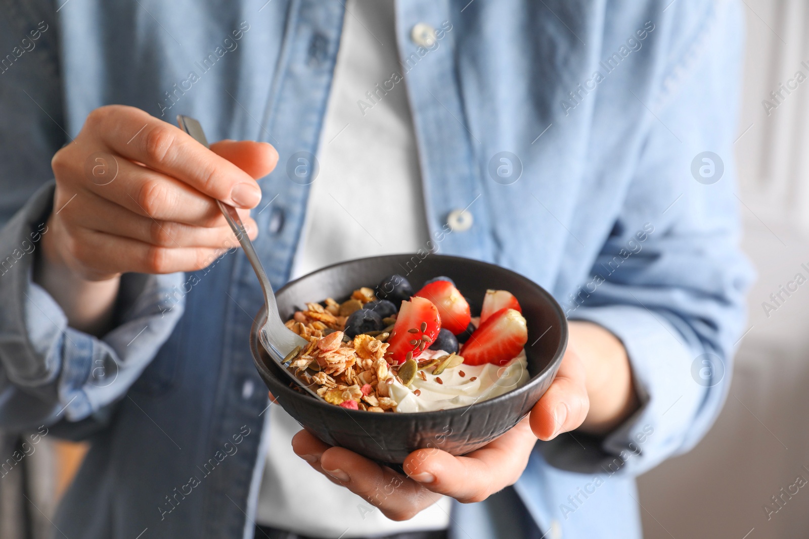 Photo of Woman eating tasty granola with berries, yogurt and seeds, closeup