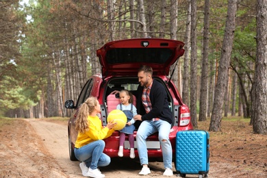 Photo of Young family with suitcases and car in forest