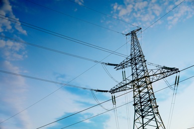 Photo of High voltage tower against blue sky on sunny day, low angle view