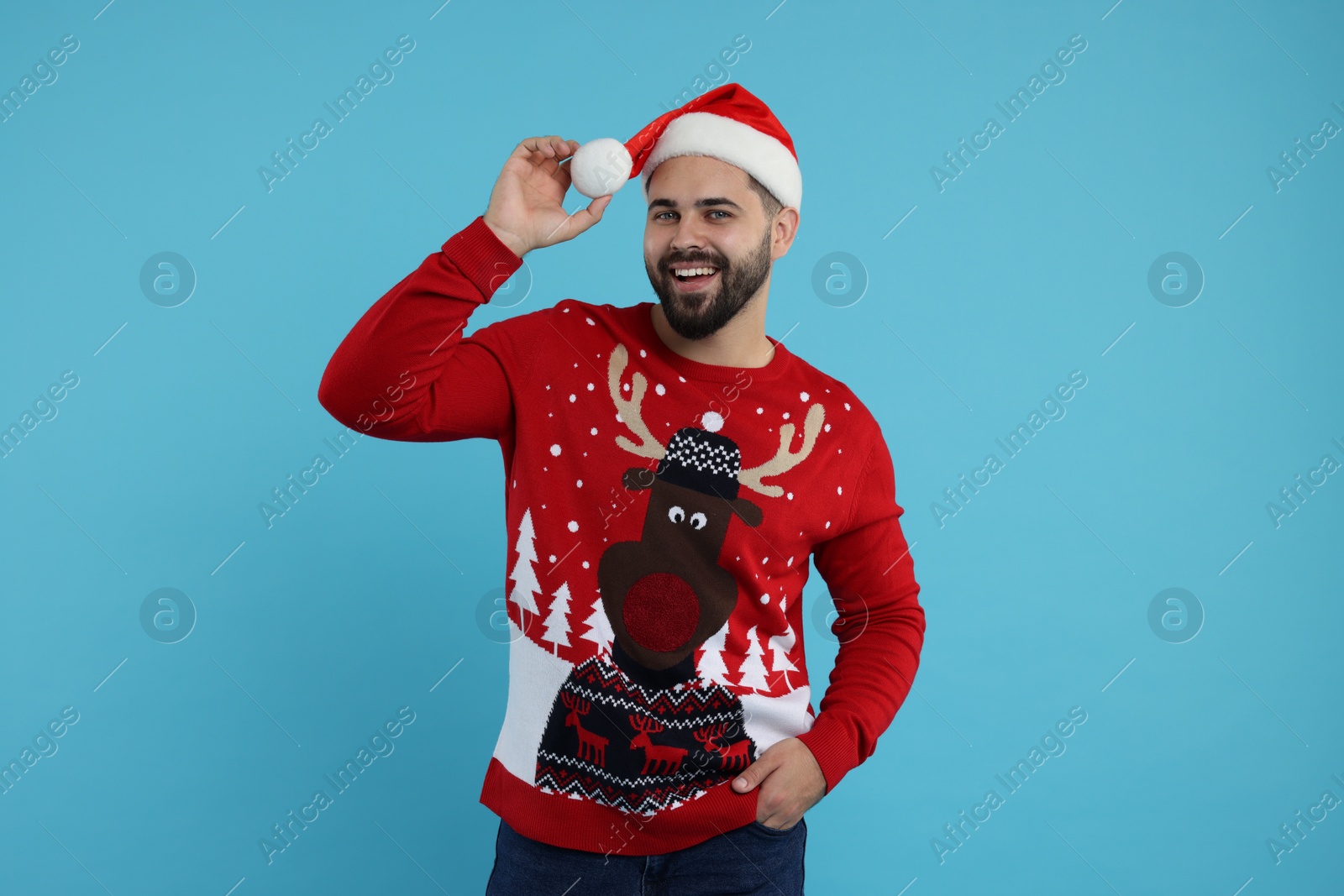 Photo of Happy young man in Christmas sweater and Santa hat on light blue background