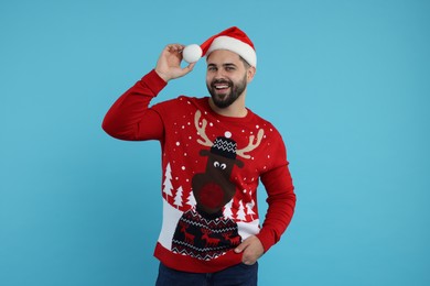 Photo of Happy young man in Christmas sweater and Santa hat on light blue background