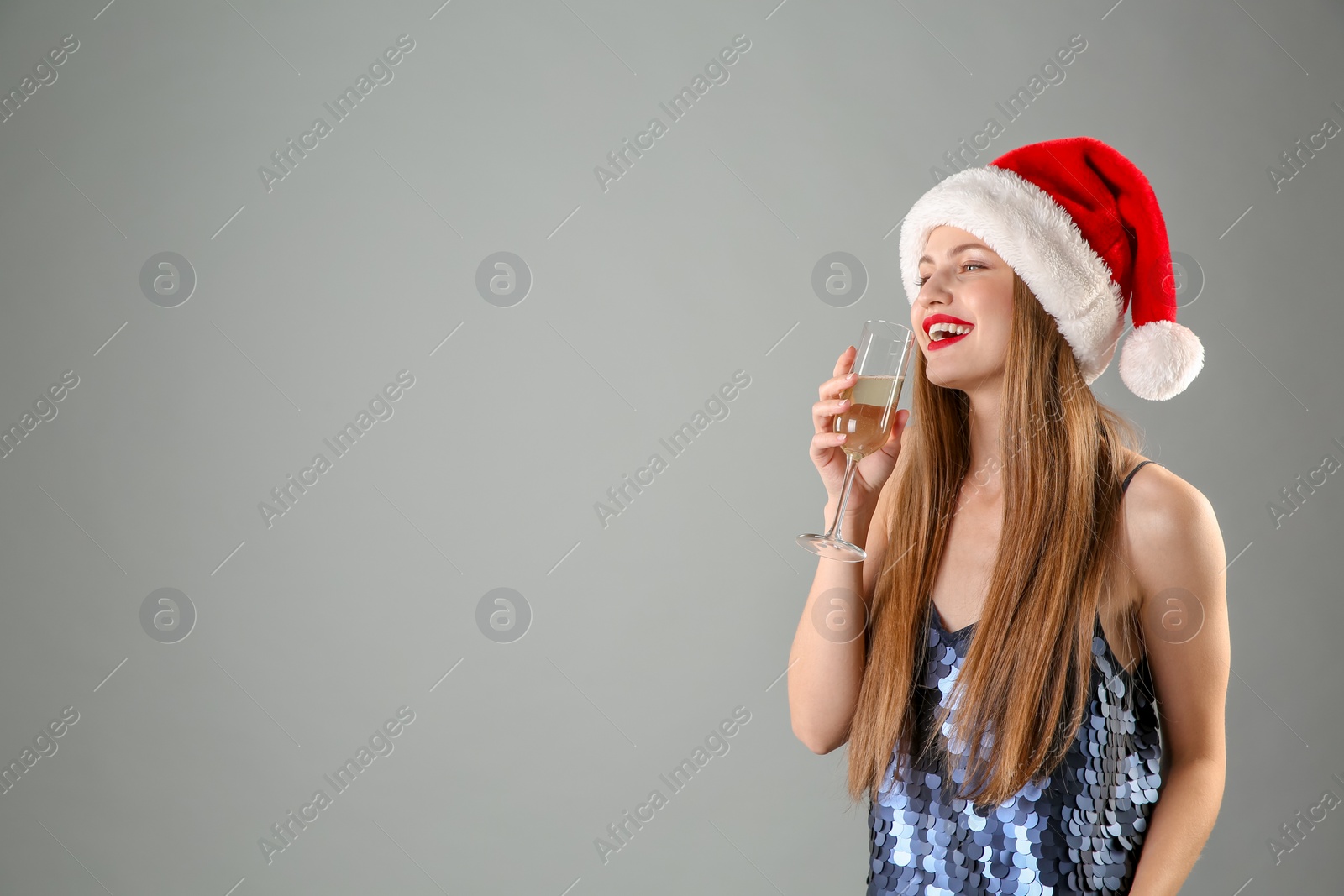 Photo of Young beautiful woman in Santa hat with glass of champagne on grey background. Christmas celebration